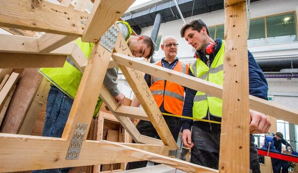Male apprentice on a mock roof construction being monitored by his tutor
